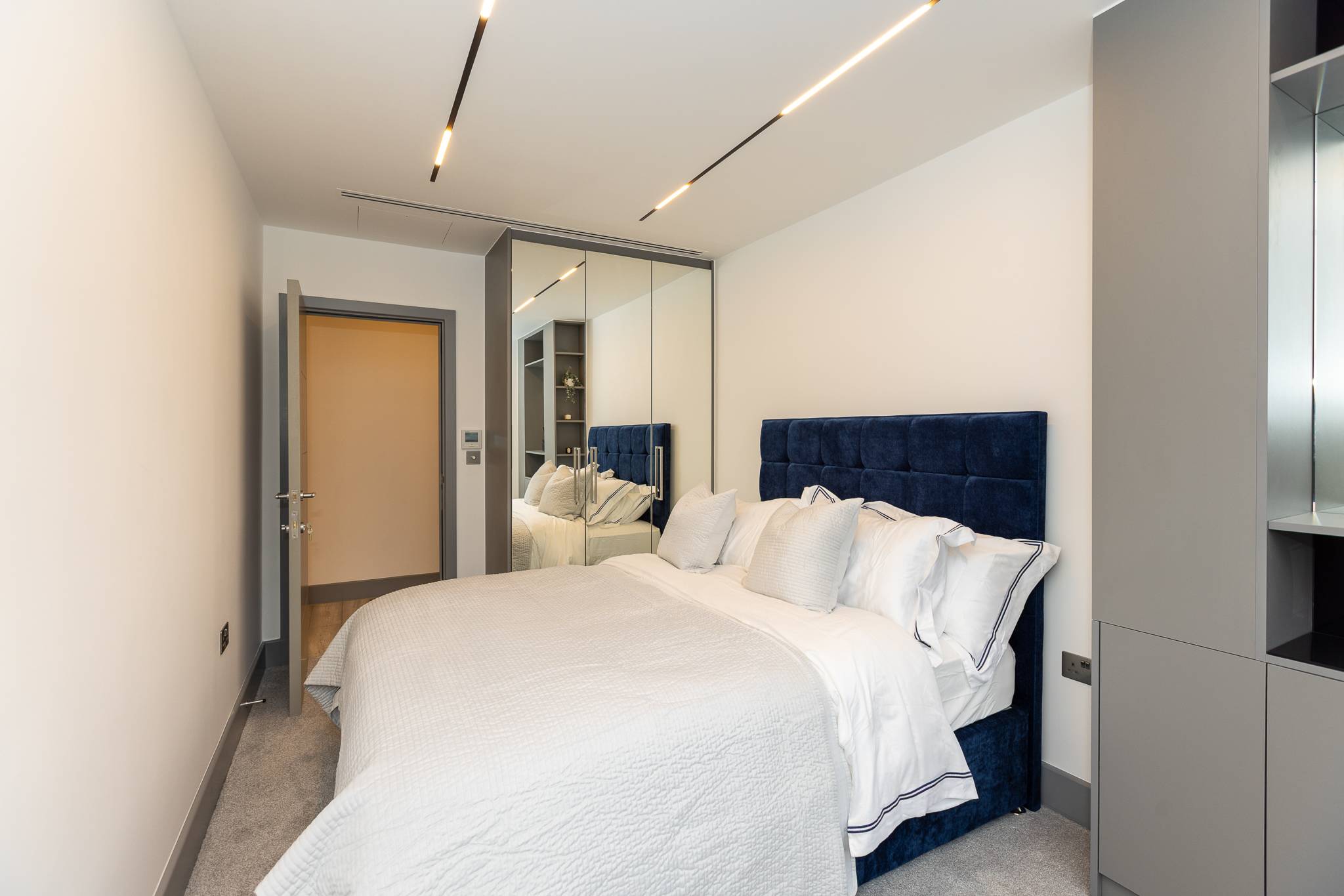 Bedroom with a navy velvet bed, white linen and a mirrored wardrobe