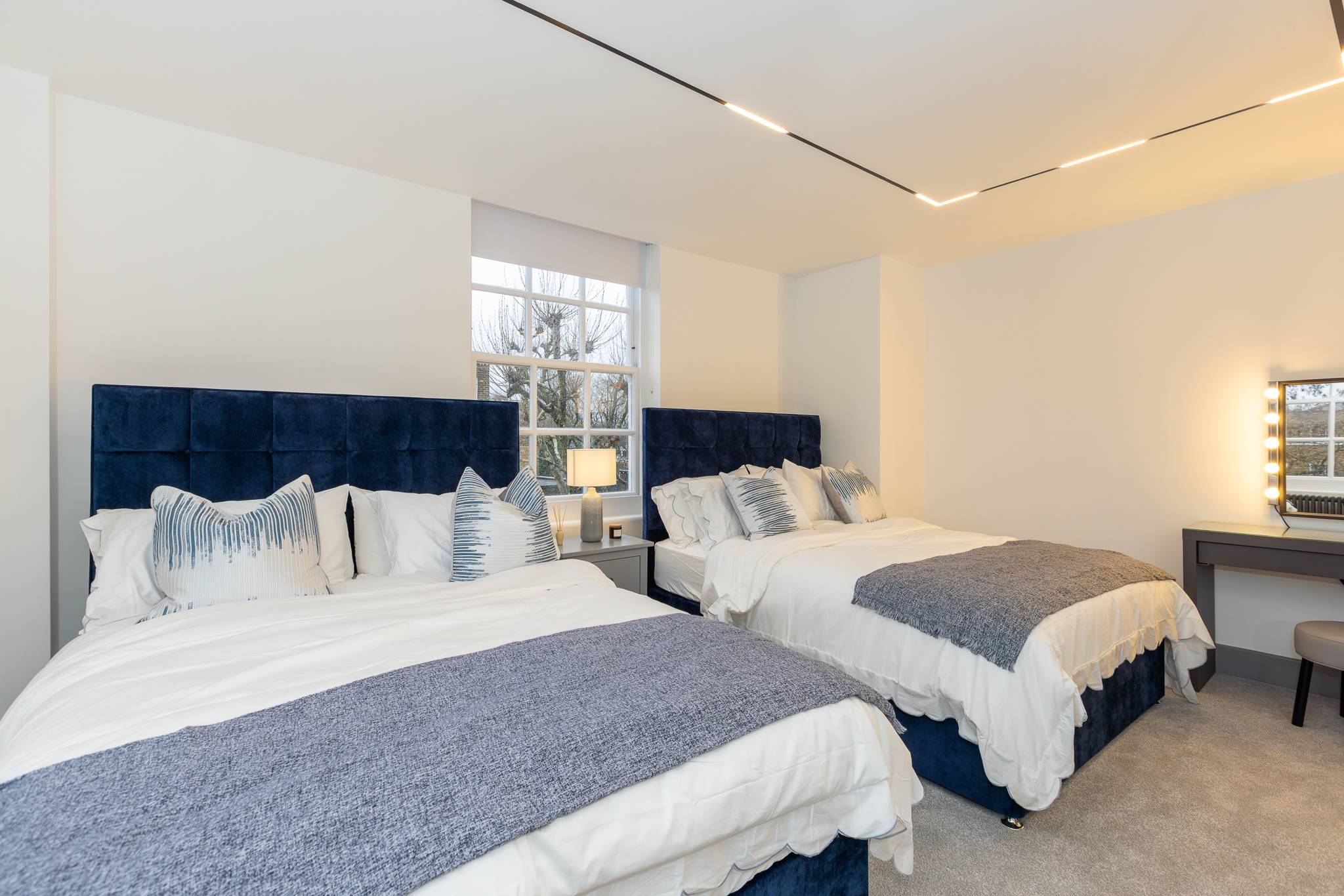Twin bedroom with two navy velvet beds and a dressing table under the window