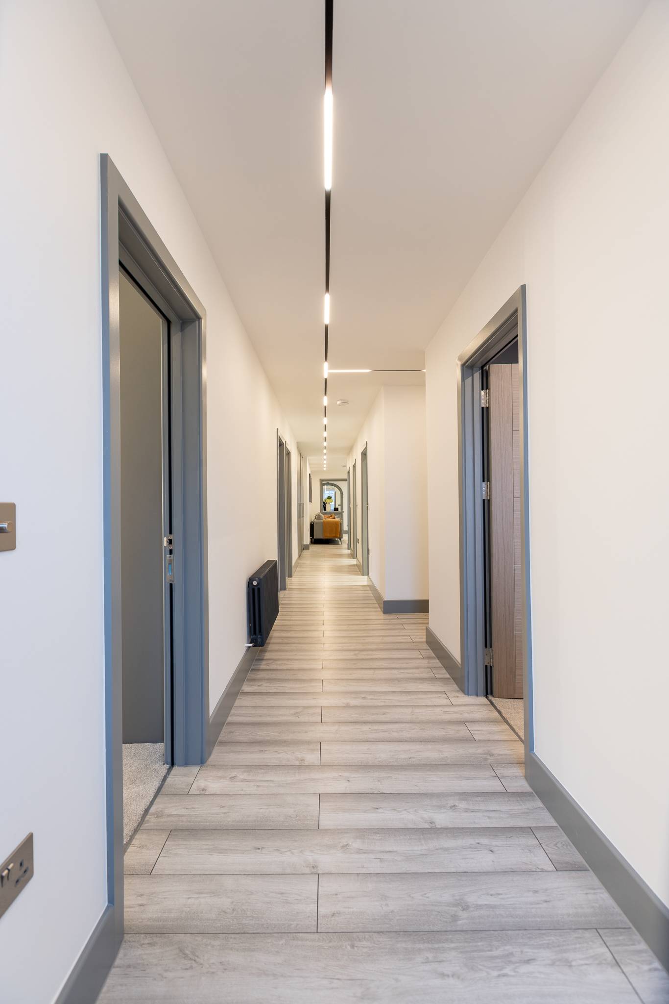 Long hallway with grey laminate flooring and a line of lights recessed in the new ceiling