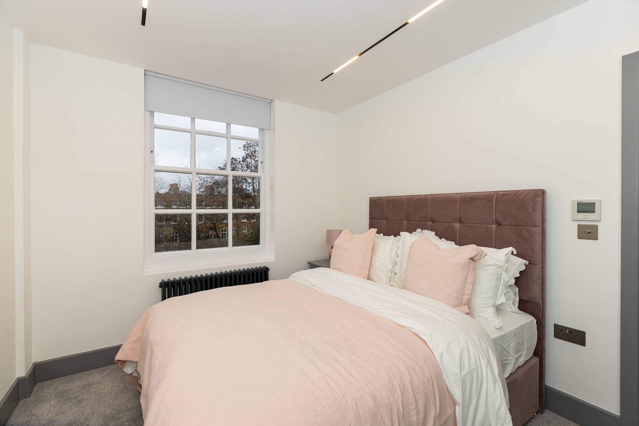 Bedroom with a blush pink upholstered bed beside a sash window