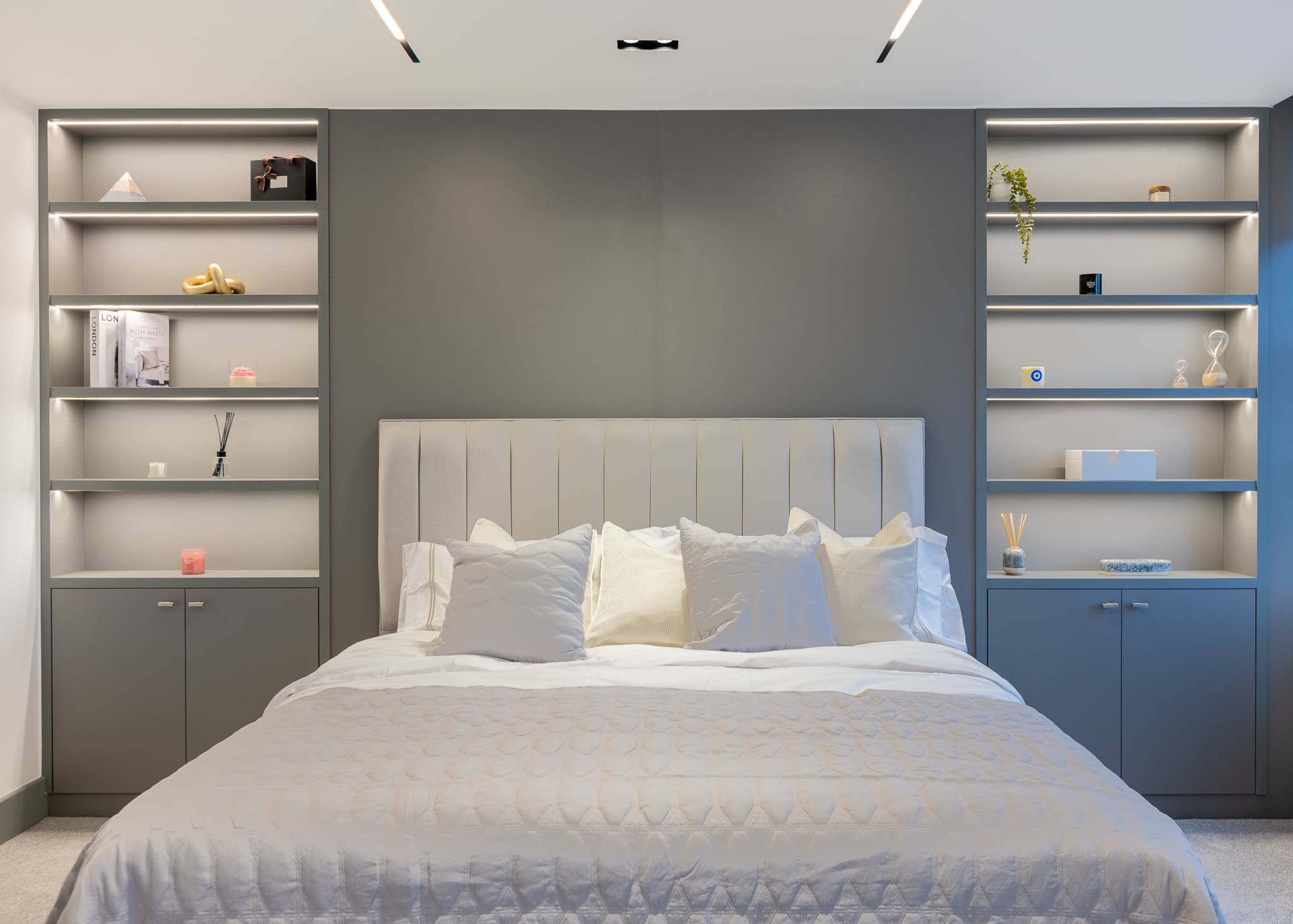Bedroom with a panelled headboard wall and lit open shelving on both sides