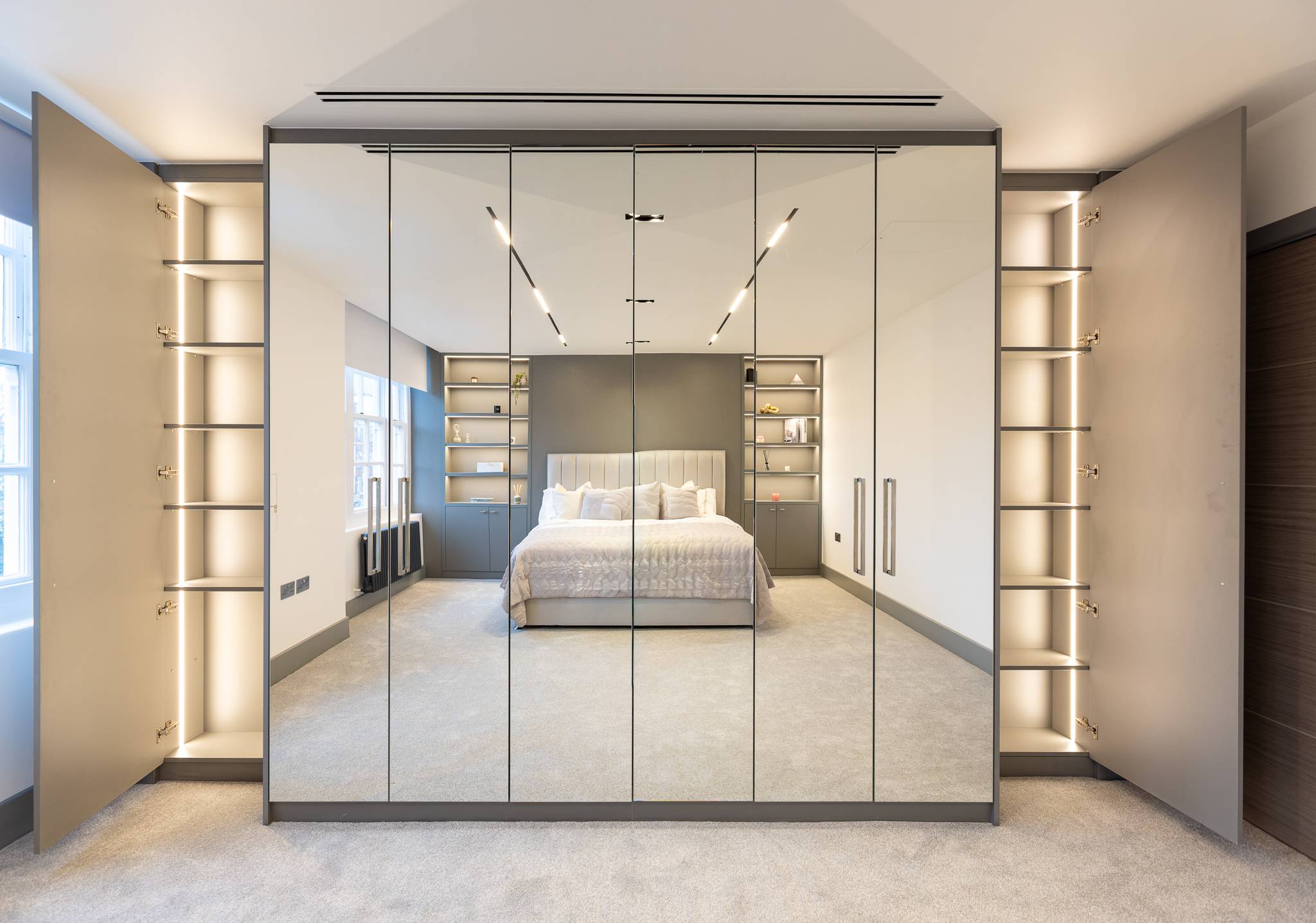 Mirrored wardrobe wall with lit open shelving at each end