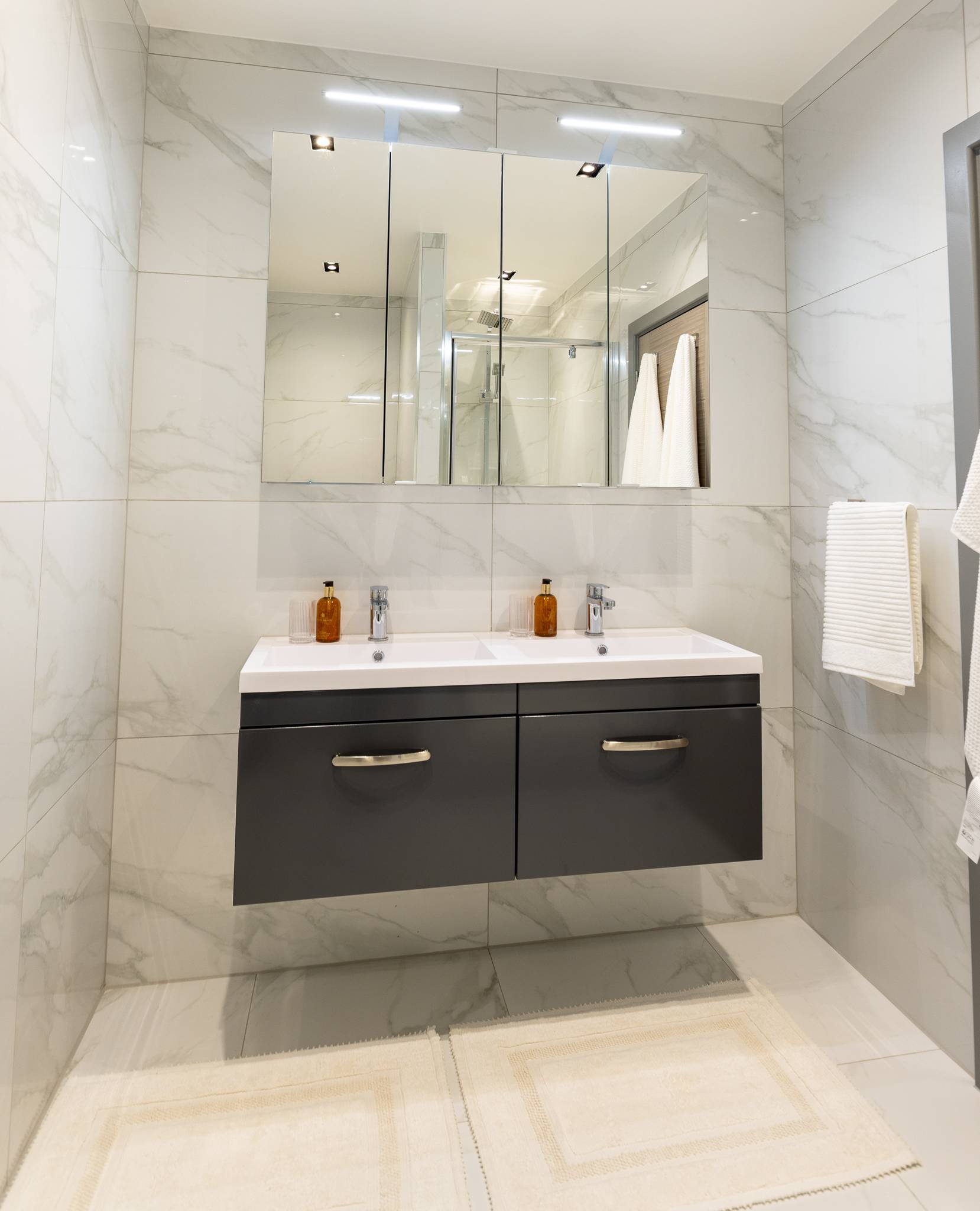 Bathroom in white marble effect tiles, with a double basin on a floating grey vanity
