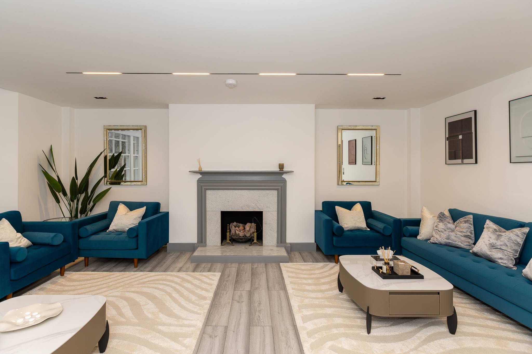 Living room with two teal velvet sofas facing a grey stone fireplace, under linear ceiling lights