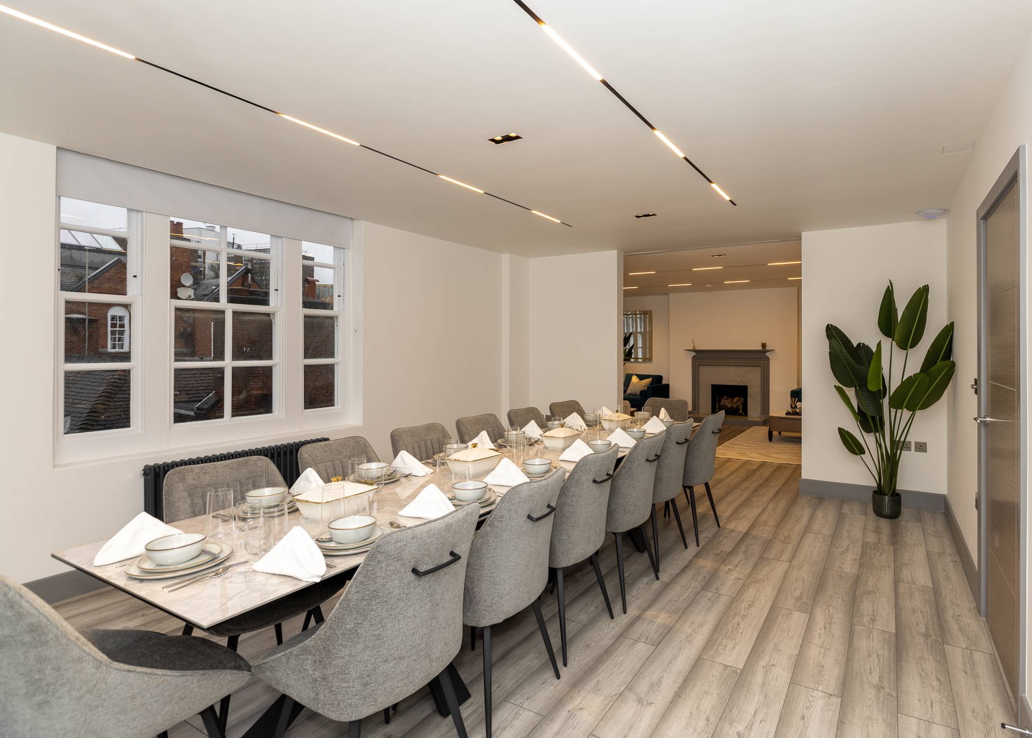 Long dining table with grey upholstered chairs and the living room beyond