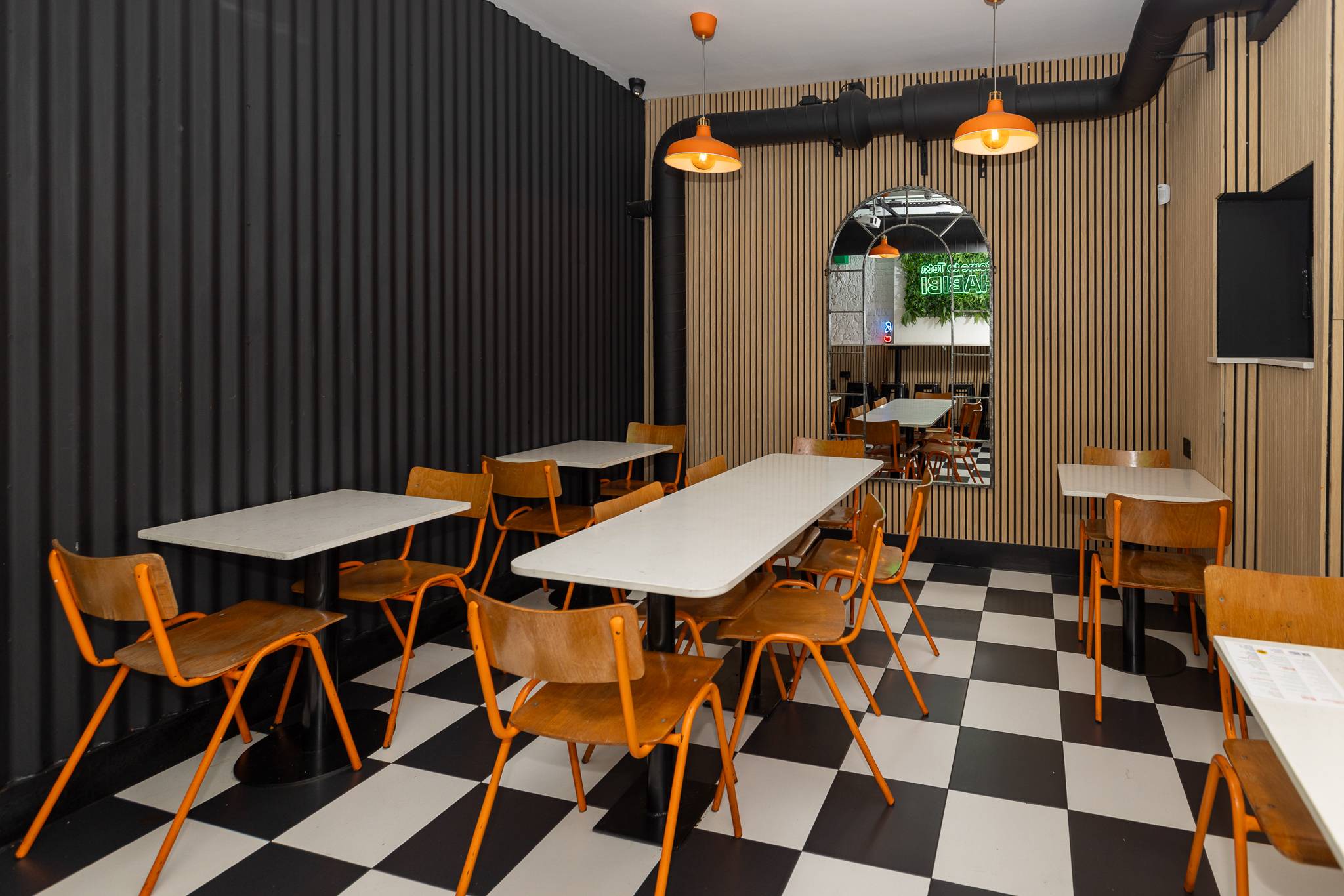Dining room at Mayyil Notting Hill with a black and white chequered floor and orange chairs