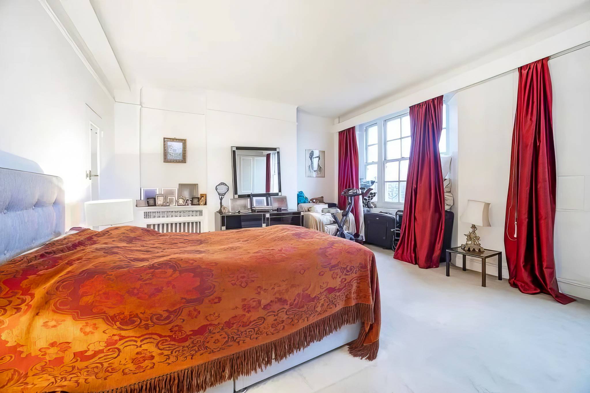 Bedroom before, lit by a single pendant, with red curtains and an old radiator
