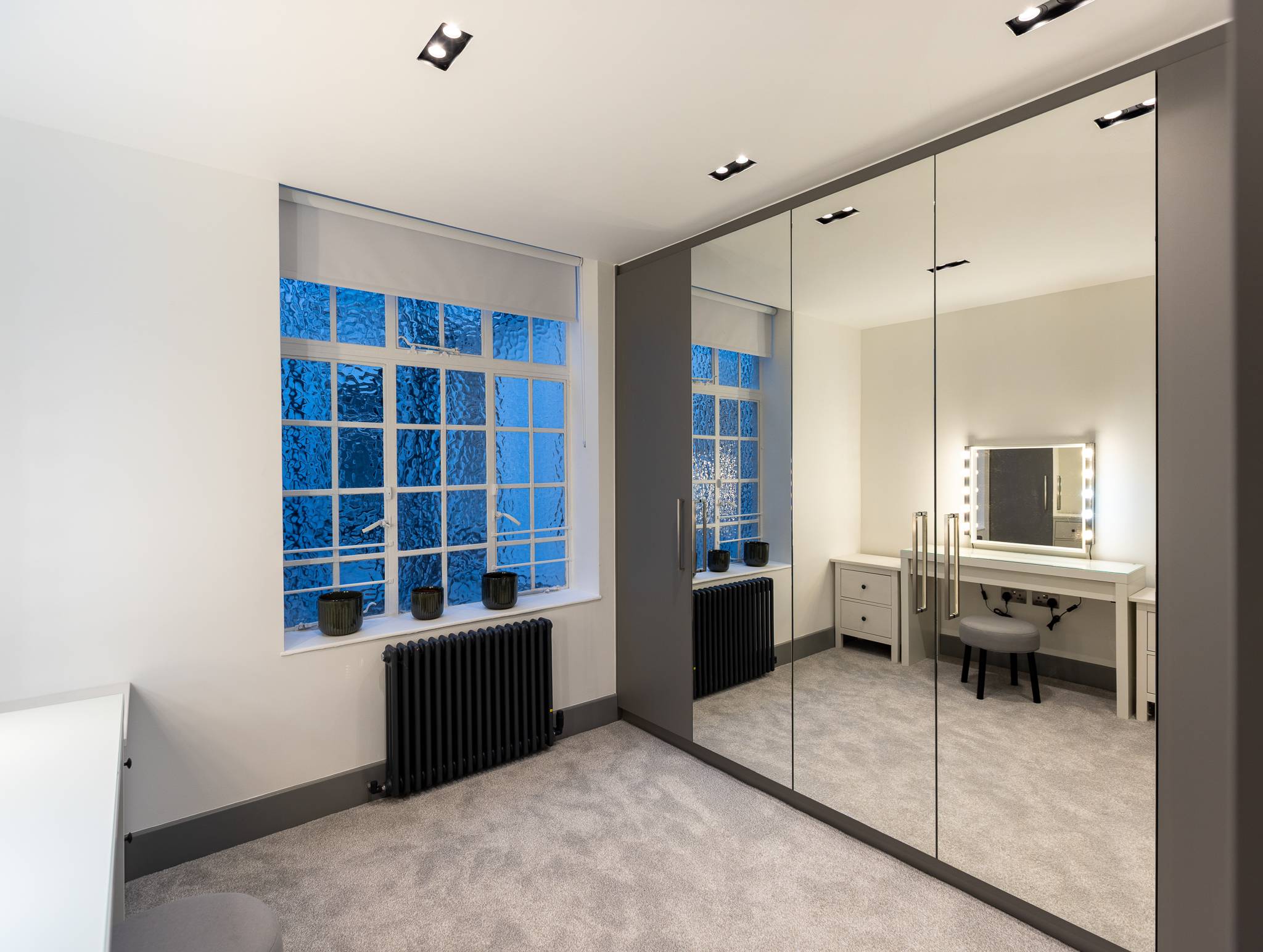 The same bedroom after, with a full height mirrored wardrobe wall and a lit dressing table