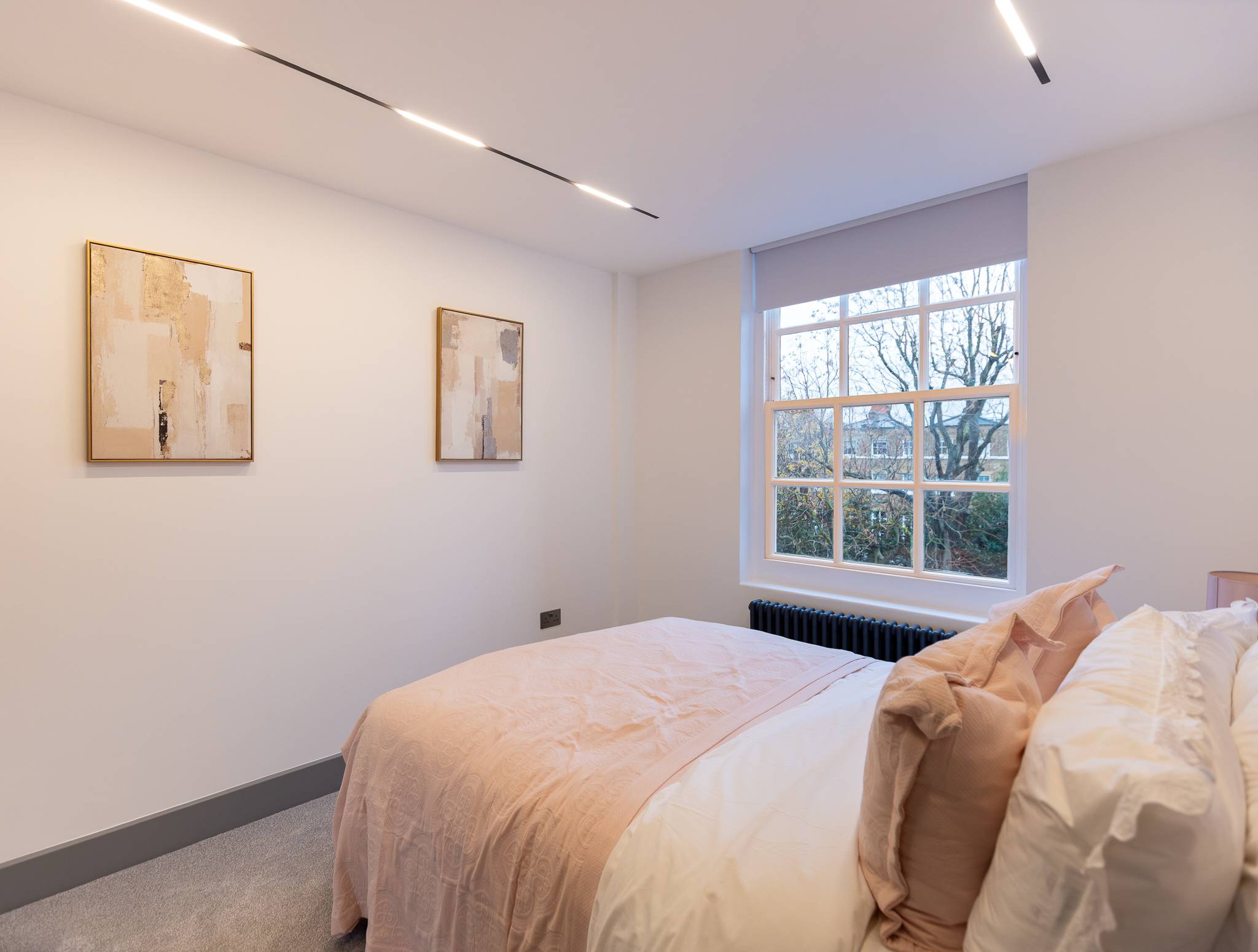 Bedroom after, with a pink upholstered bed and recessed ceiling lights