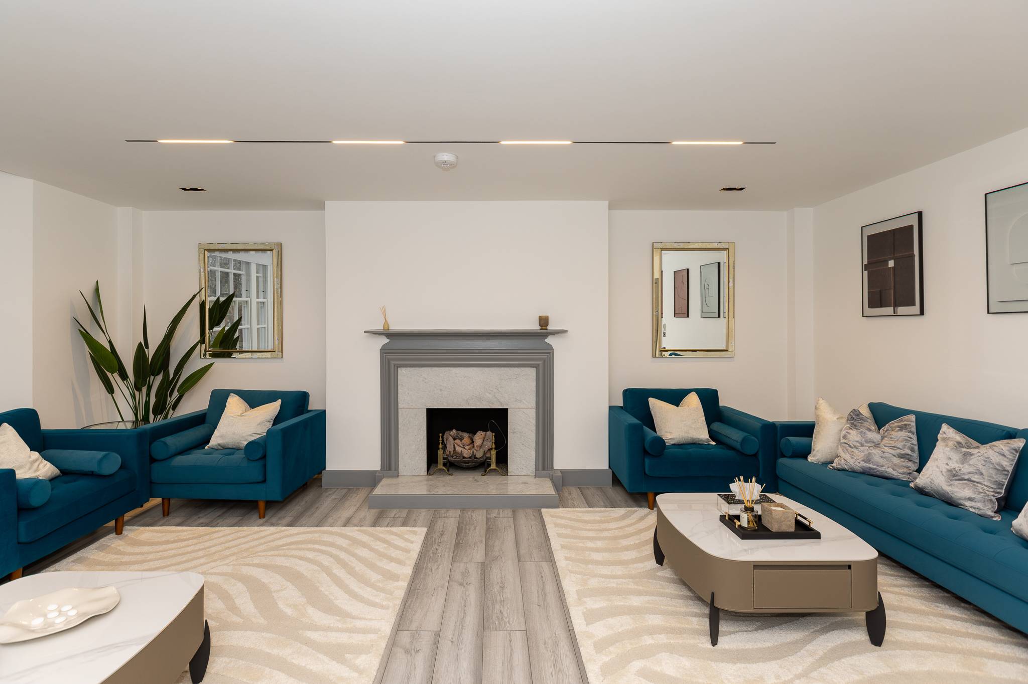Living room after, with teal velvet sofas, a grey stone fireplace and linear ceiling lights